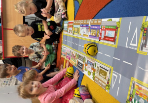 Dzieci siedzą wokół planszy, na której porusza się zaprogramowany beebot w kształcie pszczółki.