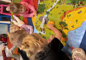 Dzieci siedzą wokół planszy z zielenią, wodospadem i wodą i programują beebota.