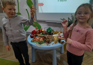 Bruno i Zuzia trzymają łańcuch ze słomy. Obok stoi stolik z ozdobami choinkowymi.