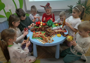 Grupka dzieci przykucnęła obok stolika i ogląda ozdoby choinkowe.