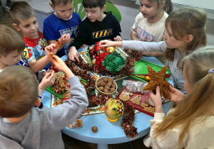 Grupka dzieci przykucnęła obok stolika i ogląda zgromadzone na nim ozdoby choinkowe.