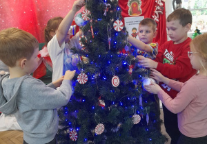 Pięcioro dzieci zawiesza bombki na choince.