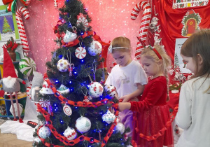 Trzy dziewczynki zawieszają łańcuch na choince.