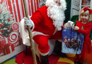 Mikołaj wręcza Emilce prezent. Z tyłu dekoracja mikołajkowa.