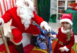 Marysia w czerwonym stroju odbiera prezent od Mikołaja.
