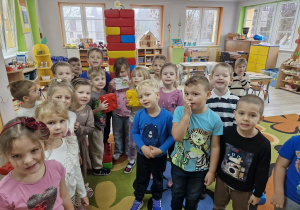 Dzieci stoją na dywanie. Za nimi widać wysoką wieżę zbudowaną z klocków. Weronika trzyma kopertę z pierwszym zadaniem od Grincha.