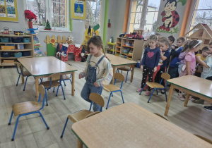 Zdzieci ustawione w pociąg idą po torze przeszkód ustawionym z krzeseł.