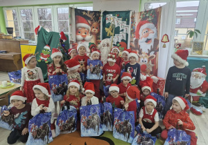 Wspólne zdjęcie dzieci z grupy Biedronek ze Świętym Mikołajem na tle świątecznej dekoracji.
