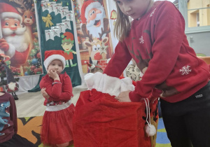 Oliwia wyjmuje prezenty z worka Świętego Mikołaja.