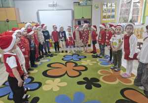 Przedszkolaki ustawione w półkole śpiewają piosenkę dla Mikołaja.