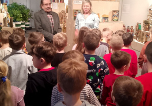 Pani etnograf i rzeźbiarz stoją przed dziećmi i opowiadają o wystawie rzeźb.