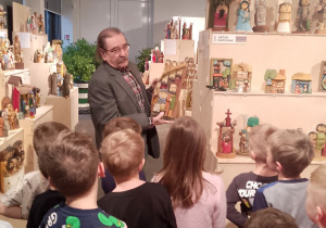 Pan rzeźbiarz trzyma w ręku rzeźbę stojąc przed dziećmi.