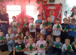 Zdjęcie grupowe z wykonanymi choinkami i instruktorkami na tle świątecznej dekoracji.