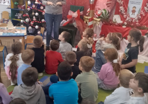 "Słoneczka" siedzą na dywanie przed nimi na tle dekoracji stoi instruktorka z Centrum Kultury Gminy Kutno.