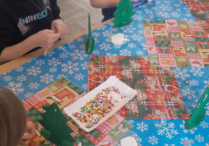 Grupka dzieci podczas dekorowania choinek cekinami.