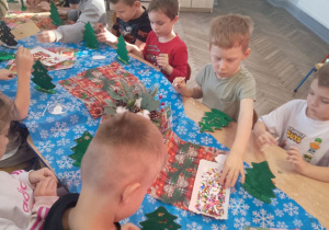 Grupka dzieci siedzi przy stole podczas dekorowania choinek.