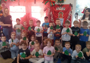 Zdjęcie grupowe z wykonanymi choinkami i instruktorkami na tle świątecznej dekoracji.