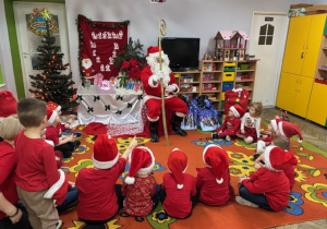 Dzieci siedzą w kole na dywanie, a Mikołaj siedzi na czerwonym krześle.