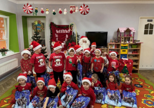 Dzieci pozują do zdjęcia z prezentami oraz Mikołajem.