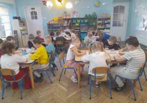 Dzieci siedzą przy stołach i kolorują obrazki o tematyce świątecznej według kodu.