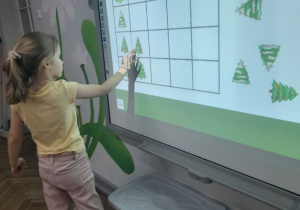 Marysia stoi przed tablicą multimedialną i układa choinkę zgodnie z kierunkiem ułożonej strzałki.