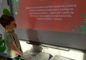 Bruno stoi przed tablicą multimedialną i czyta głośno slajd na temat wartości - rodziny.