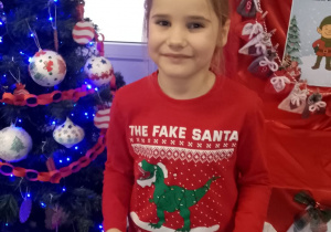 Marysia stoi przy choince trzymając swoje udekorowane pierniki na papierowej tacce.