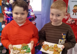 Julek i Oliwier pozują do zdjęcia ze swoimi pierniczkami przy choince.