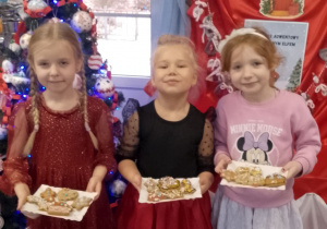 Nikola, Tosia i Emma stoją przy choince trzymając swoje udekorowane pierniki na papierowej tacce.