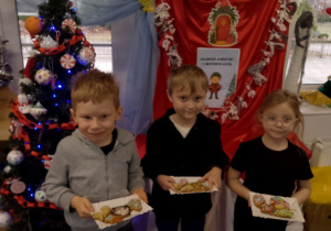 Bruno, Hubert i Zuzia pozują do zdjęcia ze swoimi pierniczkami przy choince.