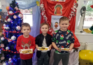 Kuba, Bartek i Marcel stoją przy choince trzymając swoje udekorowane pierniki na papierowej tacce.