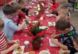 Przedszkolaki siedzą przy wspólnym stole podczas ozdabiania pierników.