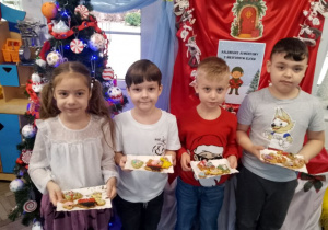Grupka dzieci pozuje do zdjęcia ze swoimi pierniczkami przy choince.