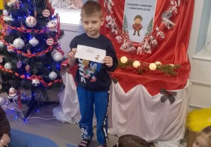 Chłopiec pokazuje zadanie dzieciom siedzącym na dywanie.