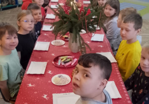 "Słoneczka" siedzą przy wspólnym stole, na którym znajduje się dekoracja świąteczna oraz pierniki, lukier i posypki.