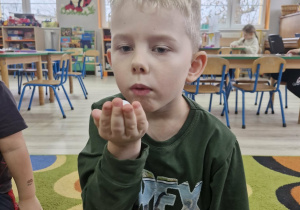 Lucjan dmucha na piłeczkę trzymaną w dłoni.