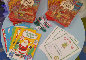 Na stoliku leżą dyplomy i nagrody dla dzieci za udział w konkursie: kolorowanki, długopisy i książki - gry dla poszukiwaczy przygód pt. "Miasto Tańczącego Karpia".