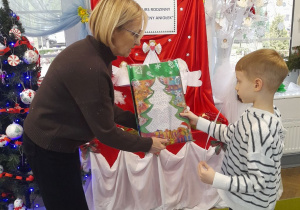 Pani dyrektor wręcza Adasiowi nagrodę w świątecznej torebce.