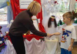 Pani dyrektor gratuluje Mikołajowi pięknej pracy i wręcza chłopcu nagrodę oraz dyplom.