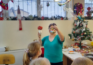 Pani prezentuje dzieciom ozdobione bombki podczas zajęć warsztatowych.