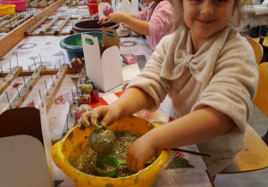 Nadia obsypuje swoją bombkę brokatem. W tle dwoje dzieci podczas pracy.