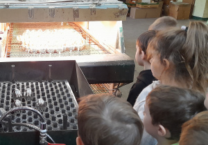 Dzieci stoją przed urządzeniem do mycia bombek oraz tunelem do suszenia.