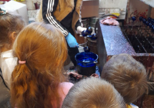 Dzieci poznają kolejny etap powstania bombek - malowanie tła. W dziale malarnia obserwują jak Pani zanurza bombki w lakierze w kolorze niebieskim.