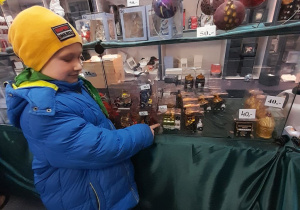 Antoś w sklepiku pokazuje bombkę w kształcie auta.