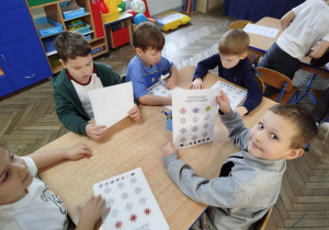 Dzieci pracują przy stoliku nad swoim dziennikiem emocji. Antoś pokazuje swoją pracę.