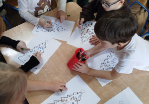 Dzieci przy stoliku wykonują pracę, która pokazuje ich preferencje świąteczne. Używają kredek do rysowania.