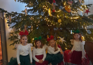 Tosia, Nadia, Marysia i Emma pozują do zdjęcia na tle choinki. Dwie dziewczynki siedzą na ławce, a dwie stoją po bokach.