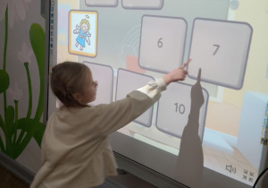 Nikola stoi przy tablicy multimedialnej i odsłania memory z aniołkami.