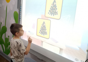 Mikołaj stoi przy tablicy multimedialnej podczas gry w memory świąteczne.