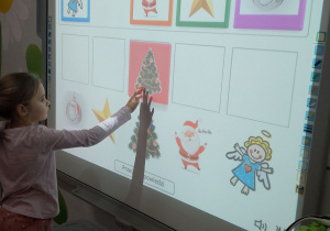 Marysia stoi przy tablicy multimedialnej i dopasowuje obrazki świąteczne do pary.